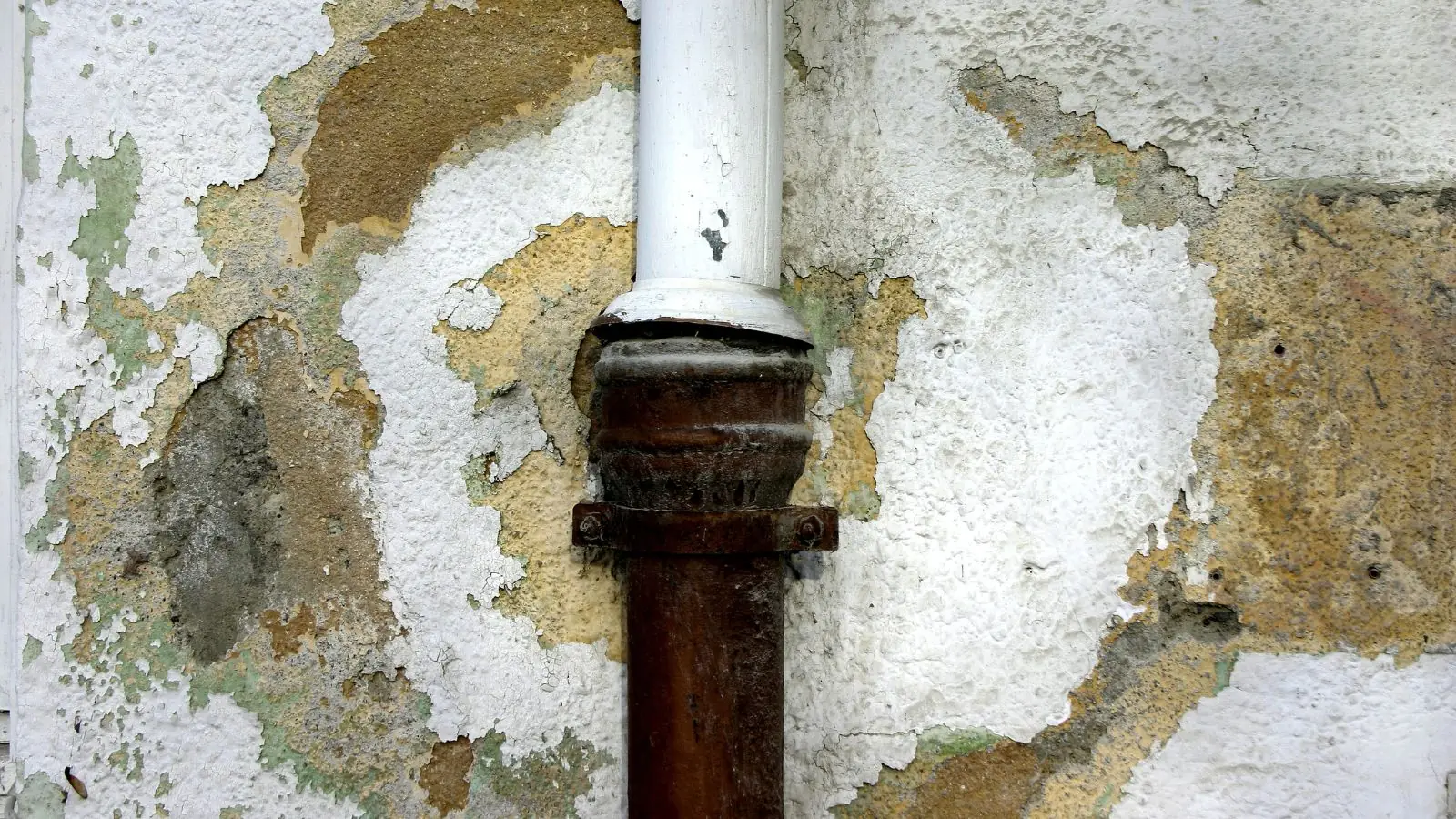 Peeling, water-stained wall plaster around a rusted drain pipe