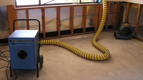 Dehumidifier with a yellow duct hose drying a room where lower wall sections were removed